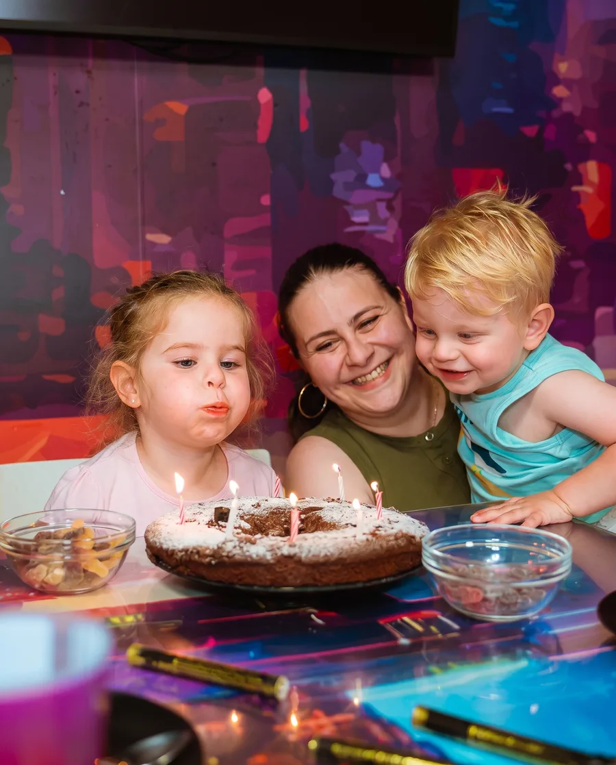 Une petite fille souffle les bougies de son gâteau, entourée de sa maman et de son petit frère