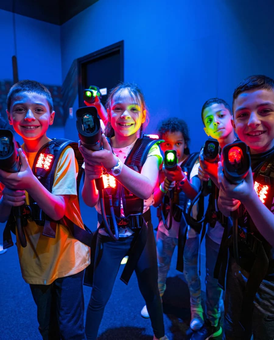 Cinq enfants tout sourire, équipés pour le laser game dans une salle éclairée aux néons